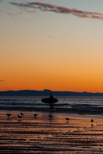 Vertical fine art surf photograph of a surfer walking on a beach in Les Landes with the Basque Coast in the background by Basile Tournier