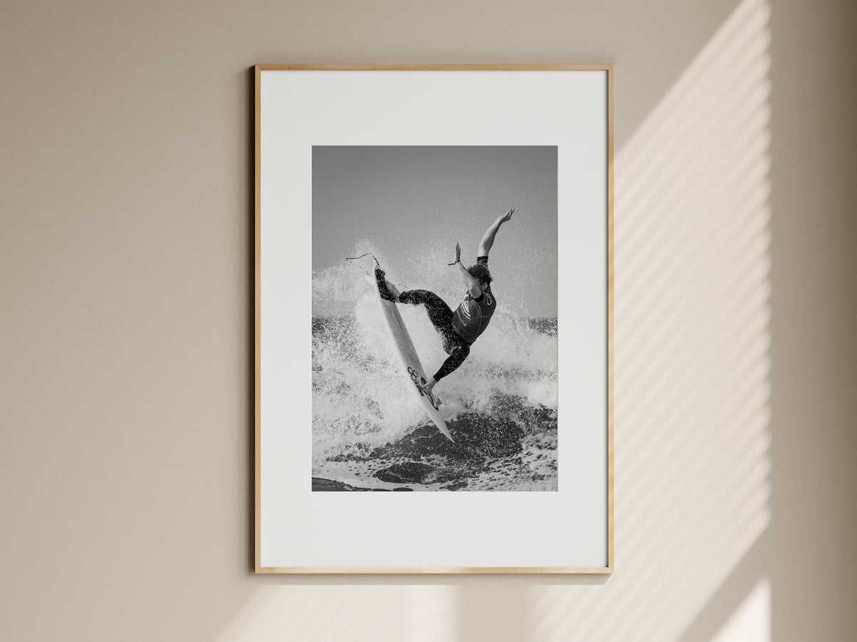 Natural oak framed black and white surf action print hanging on a beige living room wall