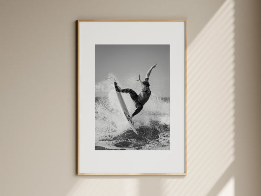 Natural oak framed black and white surf action print hanging on a beige living room wall