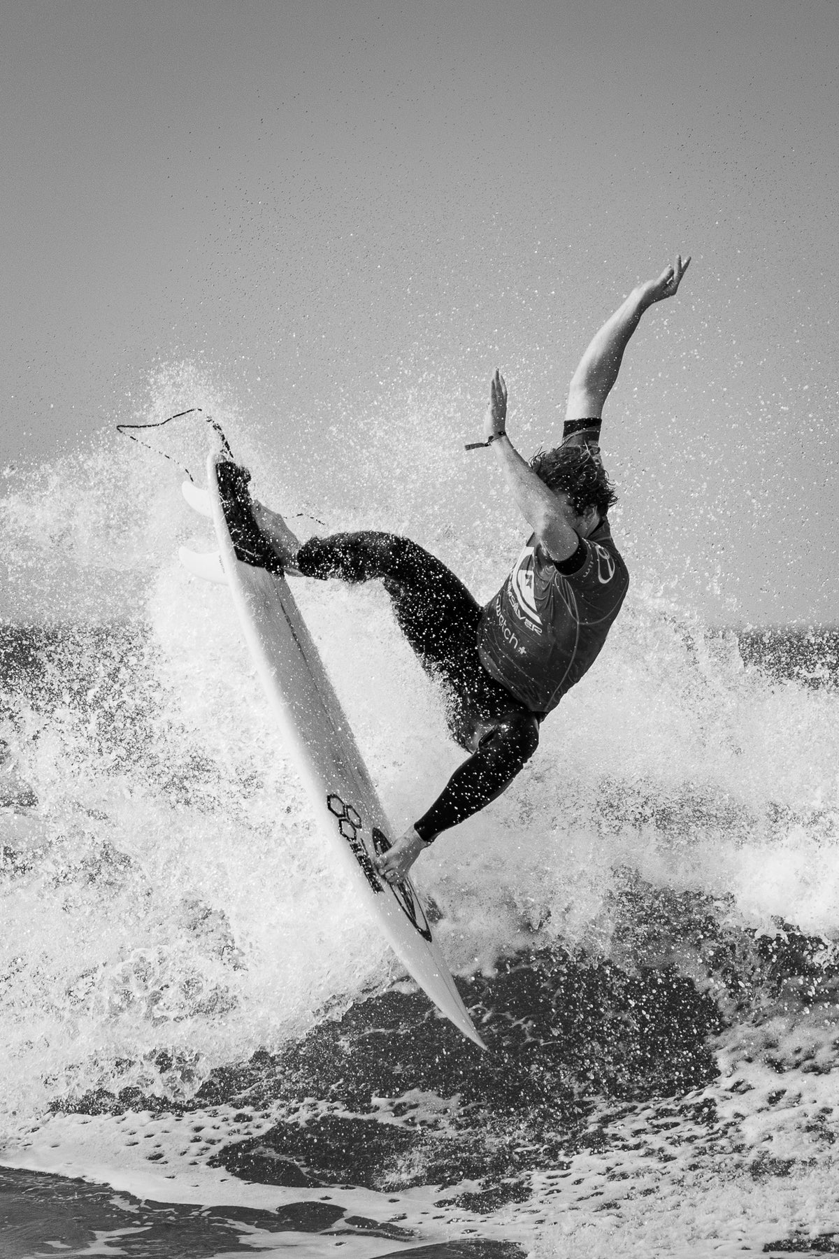 Vertical fine art black and white surf photograph of a surfer performing an aerial maneuver in Hossegor France by Basile Tournier