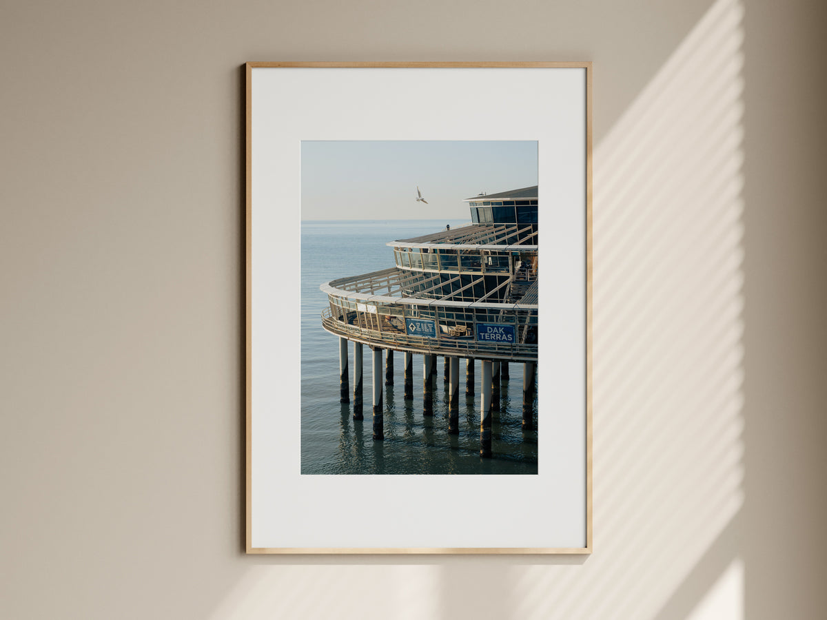 Natural oak framed fine art print of Scheveningen Pier hanging on a neutral living room wall